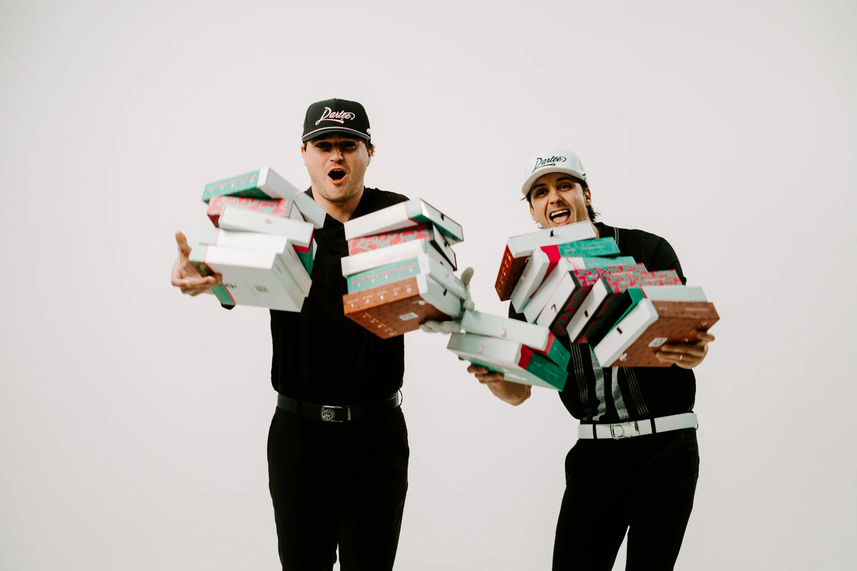 Dartee founders carrying stacks of colorful Dartee Golf belt boxes